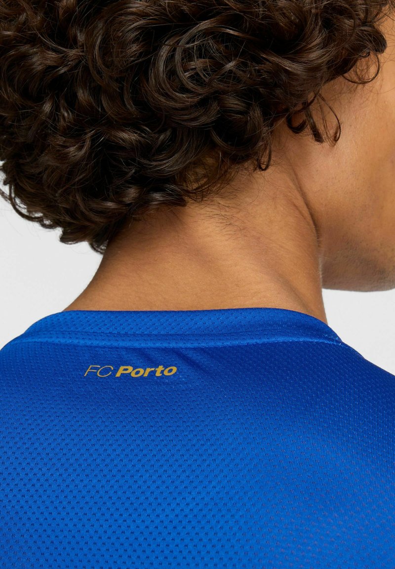Blauw sportshirt met een gestructureerde afwerking, voorzien van een ronde hals en een gouden "FC Porto"-logo op de achterkant. Close-up van het nekgebied.