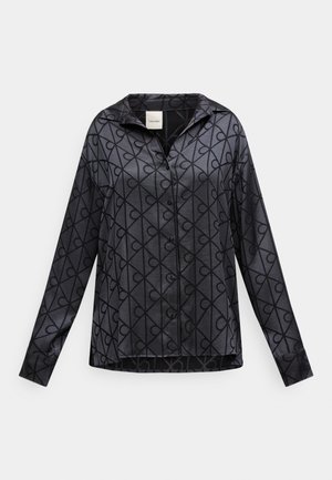 Μαύρο πουκάμισο με κουμπιά, κατασκευασμένο από γυαλιστερό ύφασμα με γεωμετρικό μοτίβο από διαπλεκόμενες γραμμές. Χαλαρή εφαρμογή με μυτερό γιακά και μακριά μανίκια.