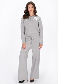 Set di loungewear grigio in maglia composto da un top corto con dettagli in paillettes e pantaloni a gamba larga con vita regolabile. Tacchi neri completano il look.