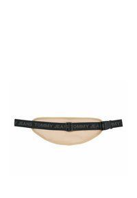 Bolso de cintura con un cuerpo de tela beige, correa ajustable negra con el logo "TOMMY JEANS" y un cierre de hebilla de plástico. Textura suave.