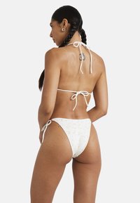Bikini bianco con motivo floreale; top con laccetto sul retro e slip con laccetto ai lati; texture a costine; copertura minima.