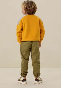 Sweatshirt jaune avec des accents d'épaule gris, pantalon cargo vert et baskets multicolores. Coupe décontractée et détails en tissu texturé.