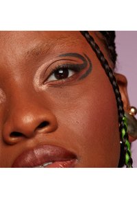 Primo piano di un volto con pelle scura, un audace design di eyeliner nero, labbra lucide e capelli intrecciati con accenti verdi e grandi orecchini.