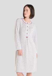 Camisa de noche blanca con pequeño estampado floral, mangas largas y cuello redondo. Presenta acentos rojos, botones y pliegues verticales en el escote.