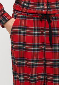 Rødeternede pyjamasbukser med elastisk talje og snor. Har hvide og sorte striber i et gittermønster. Blødt, børstet materiale.