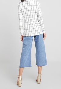 White blazer with black grid pattern, paired with light blue wide-leg cropped jeans. Gold ankle strap heels complete the look.