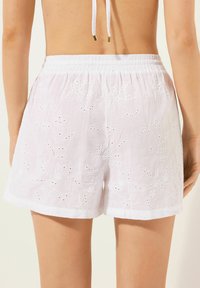 Shorts blancs brodés avec des motifs floraux, dotés d'une taille élastique froncée et de petits détails découpés à travers le tissu.