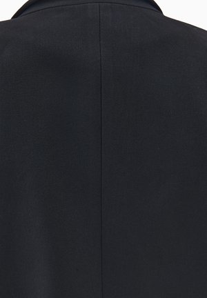 Blazer azul marino oscuro con una tela texturada. El diseño presenta un cuello estructurado y una costura trasera limpia, ofreciendo una apariencia ajustada.