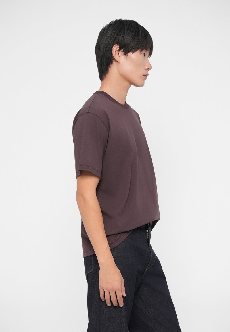 Korte mouwen, ronde hals t-shirt van diep mauve stof met een relaxte pasvorm, gecombineerd met donkere spijkerbroeken. Eenvoudig ontwerp, minimale details.