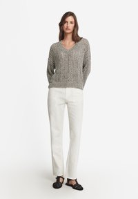 Grå stickad tröja med V-ringning, med en avslappnad passform. Tillsammans med vita raka byxor och svarta flätade sandaler.