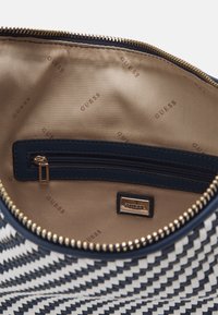 Sac à main à fermeture éclair avec un motif géométrique noir et blanc, doublé d'un tissu navy lisse, un poignet intérieur zippé et des accents en métal doré.
