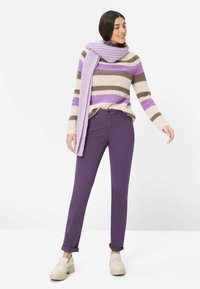 Gebreide trui met crèmekleurige, bruine en lavendelkleurige strepen, gecombineerd met paarse broek en een lichtpaarse sjaal. Lichtgekleurde plateauzolen schoenen.