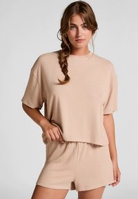 Beige katoenen top met korte mouwen en een losse pasvorm, gecombineerd met bijpassende shorts met hoge taille. Zachte textuur en minimalistische ontwerpdetails.