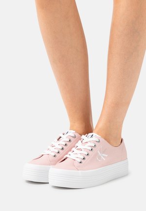 Zapatillas de lona rosa con suelas plataforma blancas y cordones, con un logo plateado en el lateral y ojales metálicos para los cordones.