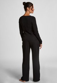 Zwarte longsleeve top met een vierkante halslijn, gecombineerd met loszittende zwarte broeken. De stof lijkt glad met minimale textuur.