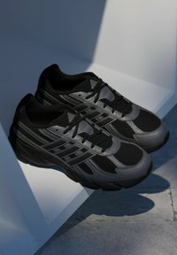 Čierne atletické topánky vyrobené z sieťoviny a syntetických materiálov s textúrovaným povrchom, s čiernymi šnúrkami a kontrastným šedým dizajnom.