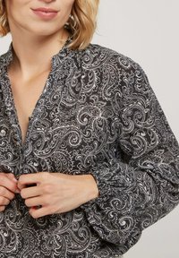 Blouse en paisley noir et blanc avec un col froncé et de longues manches bouffantes. Le tissu semble léger avec une texture lisse.