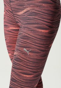 Legginsy z wzorem w kropkowe fale w odcieniach koralu i czerni, z małym srebrnym logo Pumy na udzie.