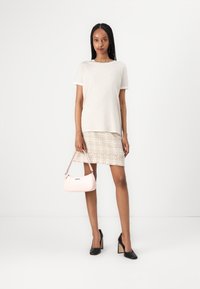T-shirt a righe chiare, gonna in tweed beige, scarpe con tacco a blocco nere e una piccola borsa rosa. Materiali texturizzati con linee pulite.