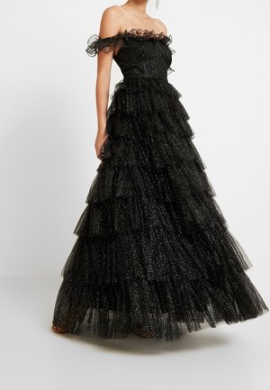 Zwarte off-shoulder baljurk met gelaagde ruches en glinsterend stippenpatroon, nauwsluitend lijfje met delicate gerimpelde halslijn.