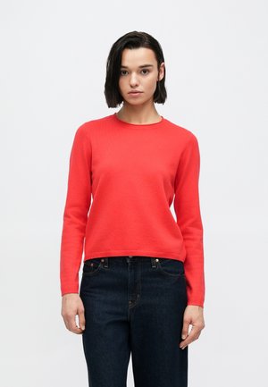 Suéter de punto rojo con cuello redondo, mangas largas y cintura ajustada, combinado con jeans de mezclilla oscura. La textura parece suave y lisa.