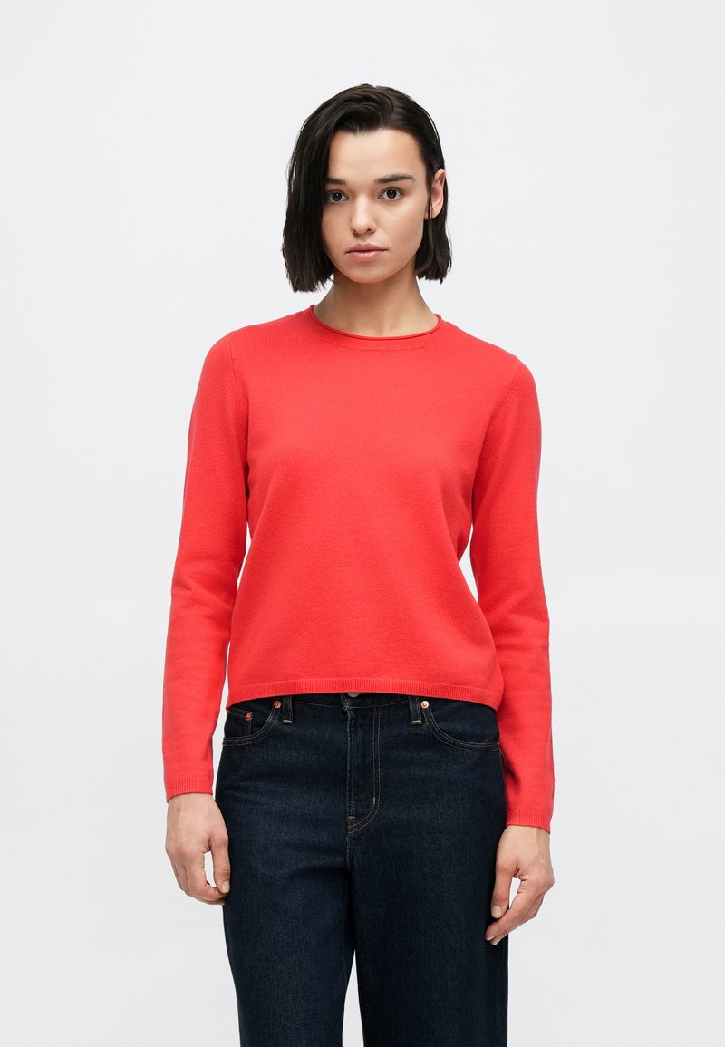 Suéter de punto rojo con cuello redondo, mangas largas y cintura ajustada, combinado con jeans de mezclilla oscura. La textura parece suave y lisa.