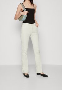 Jeans blancos acampanados con cinco bolsillos, diseñados con una cintura alta y costuras sutiles. Combinados con una camiseta sin mangas negra y bailarinas negras.