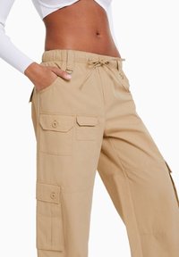 Lichte, khaki cargobroek met een elastische tailleband, koord en meerdere zakken met knoopsluitingen en platte naden.