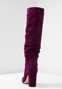 Bota de gamuza morada hasta la rodilla con un diseño holgado, que cuenta con un alto tacón cuadrado y un acabado suave y texturizado.