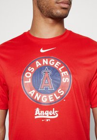 Camiseta roja de Nike con un logo circular de los Angeles Angels sobre un fondo azul, enmarcado con un borde de color y texto blanco.