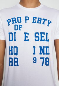 White cotton t-shirt with blue distressed text reading "PROPERTY OF DIESEL HQ IND. 978". Short sleeves, crew neck, regular fit.