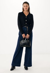 Cardigan nero con bottoni, jeans blu scuro a gamba larga e una piccola borsa nera in pelle di cocodrillo stampata con dettagli e manici dorati.