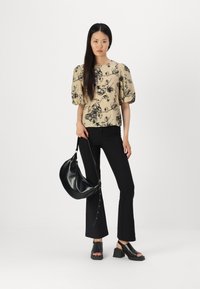 Blomsterprydd beige topp med puffermer, parret med svarte flagrende bukser og en svart lærveske. Svarte blokkhelede sandaler fullfører antrekket.
