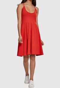 Robe rouge sans manches avec un décolleté arrondi, un corsage ajusté et une jupe évasée. Fabriquée en tissu doux, associée à des baskets blanches.