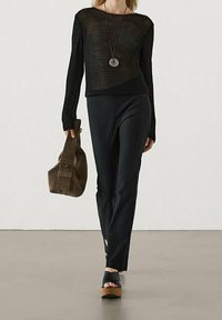 Black knitted long-sleeve top, fitted black trousers, platform sandals, and gray slouchy bag. Notable round pendant necklace.