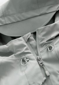 Veste imperméable gris clair avec capuche, fermeture éclair avant partiellement ouverte, et cordons de serrage réglables près du col.