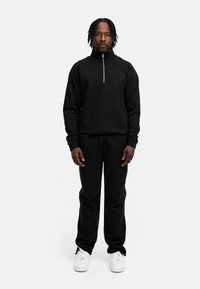 Black zip-up sweatshirt with high collar, paired with black sweatpants. White sneakers complete the look. Smooth texture, relaxed fit.