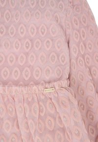 Abito rosa con tessuto testurizzato e motivo a diamante, arricchito da dettagli luccicanti. Vita arricciata con una piccola etichetta di marca.