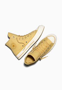 Baskets montantes en cuir jaune avec semelles en caoutchouc blanches et œillets, présentant un logo circulaire et une tige texturée.