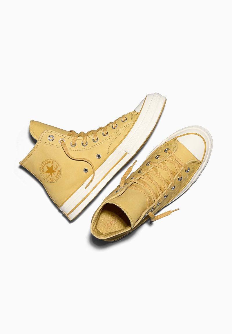 Hohe gelbe Ledersneaker mit weißen Gummisohlen und Ösen, mit einem runden Logo und einer strukturierten Oberseite.