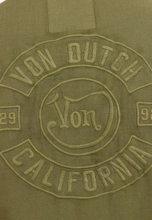 Præget olivengrønt stofmærke med teksten "Von Dutch California" og numrene "29" og "93" i dekorativ stil.