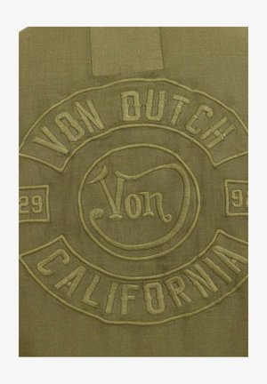 Præget olivengrønt stofmærke med teksten "Von Dutch California" og numrene "29" og "93" i dekorativ stil.