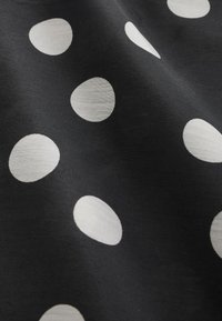 Tissu noir avec des pois blancs irréguliers répartis sur la surface, montrant la texture et de légers plis.