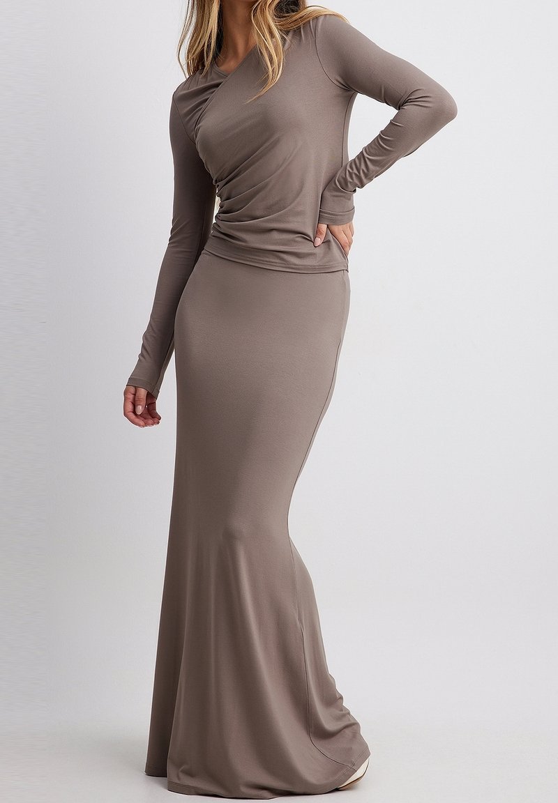 Langes, enganliegendes Kleid aus weichem, elastischem Material in einem gedämpften Braunton. Verfügt über lange Ärmel und ein drapiertes Dekolleté-Design.