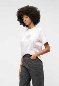 Ljusrosa bomullströja med rund hals och broderad logga. Matcher med mörkgrå jeans med blommönster och hjärtan.