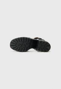 Schwarze Gummisohle mit strukturiertem Profil, das Rillen und Muster für besseren Grip aufweist. Minimalistisches Design, robuste Struktur und flaches Profil.