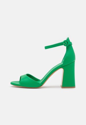 Green high-heeled sandal with an open toe and ankle strap. Features a block heel and smooth leather-like texture.
