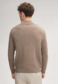 Brauner Strickpullover mit texturierter Optik, versehen mit einem klassischen Kragen und gerippten Bündchen, von hinten vor einem hellen Hintergrund dargestellt.