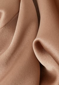 Zacht, blush-kleurig stof met een gladde textuur, die gedrapeerde plooien en een subtiele glans toont, wat de lichtgewicht en delicate aard benadrukt.
