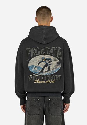 Black hooded sweatshirt featuring a graphic print of a skier and text "PEGADOR WINTERSPORT Whispers of Cold" on the back.